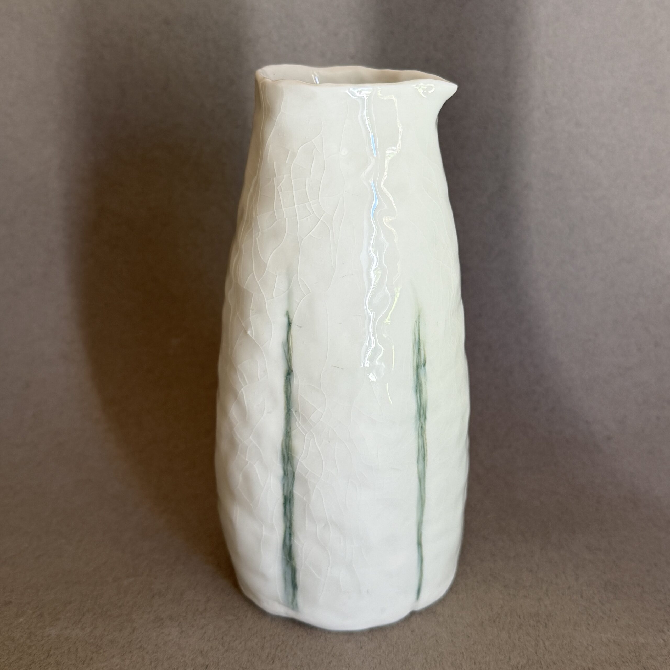 Pichet en porcelaine avec des lignes vertes et à la forme florale façonné à la main par la céramiste Martha Stahlkopf dans son atelier à Strasbourg.