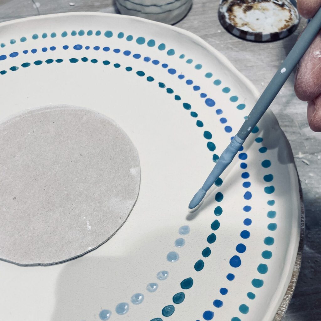 La céramiste Martha Stahlkopf, à Strasbourg, en train de décorer une assiette en porcelaine blanche et bleue.